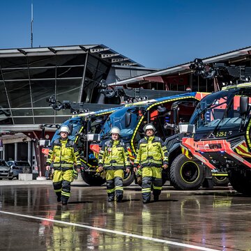 Feuerwehrteam mit Schutzkleidung vor modernen Löschfahrzeugen am Flughafen Stuttgart
