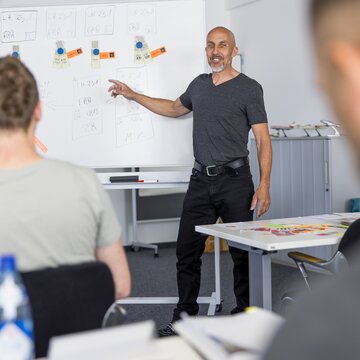 Ein Ausbilder erklärt an einem Whiteboard Inhalte vor mehreren Teilnehmenden in einem Schulungsraum am Flughafen Stuttgart.