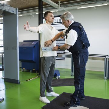 Personenkontrolle am Flughafen Stuttgart Sicherheitsmitarbeiter kontrolliert einen Passagier mit Handscanner im Sicherheitsbereich des Flughafens Stuttgart.