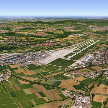Luftaufnahme des Flughafens Stuttgart mit Start- und Landebahn, Terminals und umliegenden Feldern und Ortschaften an einem klaren Tag.